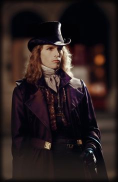 a man with long hair wearing a top hat and purple coat, standing in front of a building