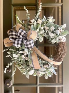 a wreath hanging on the front door decorated with greenery and burlucks