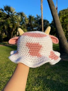 a hand wearing a pink and white crocheted cow hat