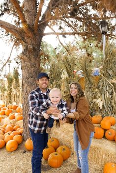 a man and woman holding a baby in front of pumpkins