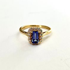 a gold ring with a blue stone surrounded by white and yellow diamonds on a white surface