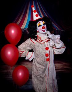 a clown dressed in white and red is posing for the camera with balloons behind him