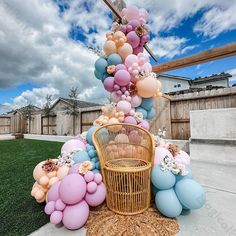 a wicker chair sitting on top of a grass covered yard next to balloons and flowers