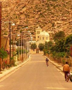 two people walking down the street in front of a mountain