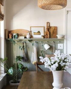 a wooden table topped with white flowers next to a shelf filled with potted plants