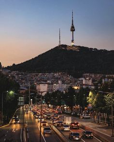 cars are driving down the street in front of a hill with a spire on top