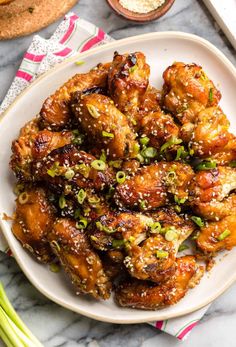 chicken wings with sesame seeds and green onions on a white plate next to some bread