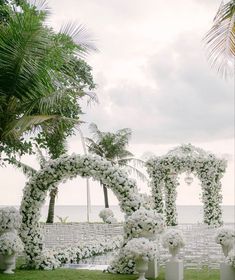 an outdoor ceremony setup with white flowers and greenery on the grass, surrounded by palm trees