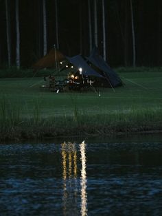 a tent is set up on the bank of a lake at night with its lights on