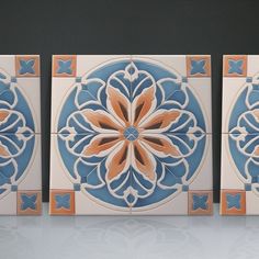 three tiles are shown in different colors and designs on the wall, one is blue with an orange flower