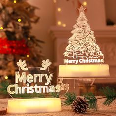 two lighted christmas trees sitting on top of a table next to a christmas tree and pine cones