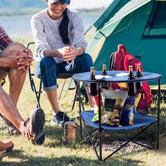 two people sitting in chairs next to a table with bottles of wine on it near a tent