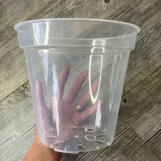 a person's hand holding up a plastic cup with scissors in it on a wooden floor