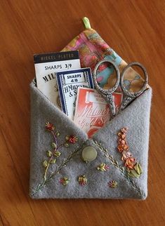 an envelope with scissors and other items in it sitting on a wooden table next to a pair of eyeglasses