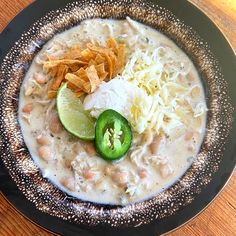 a black plate topped with soup and chips on top of a wooden table next to a green pepper