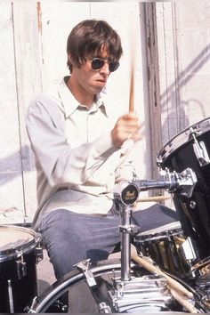 a man sitting on top of a drum set holding a stick in his hand and wearing sunglasses