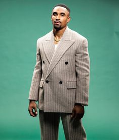 a man wearing a suit and standing in front of a green background with his hands in his pockets