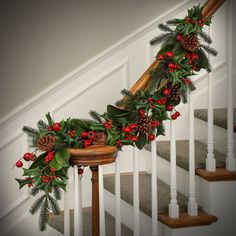 a christmas garland on the banister with pine cones and holly berries hanging from it