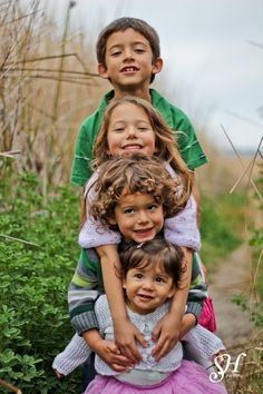 three children are sitting on top of each other in front of tall grass and bushes