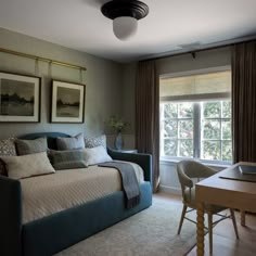 a bed sitting in the middle of a bedroom next to a table and chair with two framed pictures on it