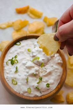 a hand holding a tortilla chip and dipping it into a bowl of dip