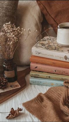 a stack of books sitting on top of a bed next to a vase filled with flowers