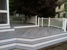 a deck with white railings and steps leading up to the front door on a house