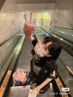 a woman wearing a face mask while riding an escalator with a drink in her hand