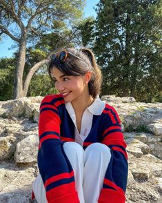 a woman sitting on top of a rock next to trees