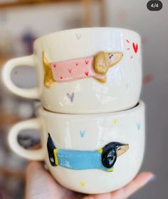 two coffee mugs with dogs on them are being held by someone's hand