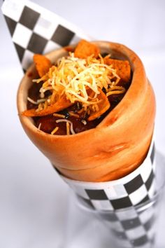 a wooden bowl filled with chili cheese and tortilla chips on top of a checkered table cloth