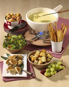 a table topped with plates and bowls filled with food next to bread sticks, grapes and cheesesticks