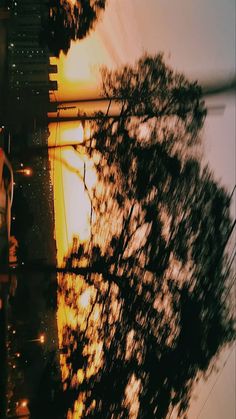 the sun is setting behind some trees in front of a street sign and building with cars parked on it