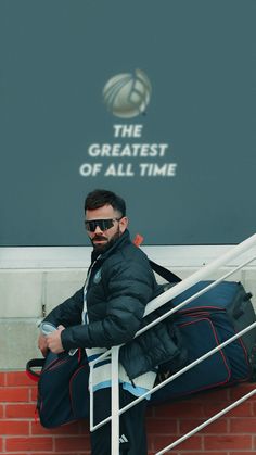 a man sitting on top of a stair case next to a wall with a sign that says the greatest of all time