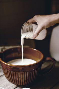 a person pouring milk into a brown bowl