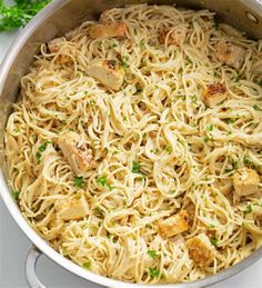 pasta with chicken and parsley in a pan on a white counter top, ready to be eaten