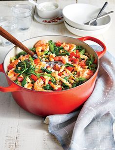 a red pot filled with shrimp, broccoli and carrots on top of a table