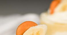 a close up of a banana on a spoon with whipped cream in the back ground