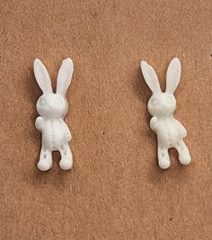 two white plastic rabbits sitting on top of a brown surface