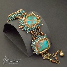 an ornate bracelet with turquoise beads and gold accents on a black background, sitting on top of a cardboard box