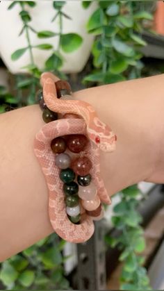 a woman's arm with a snake and beads bracelet on it, next to a potted plant