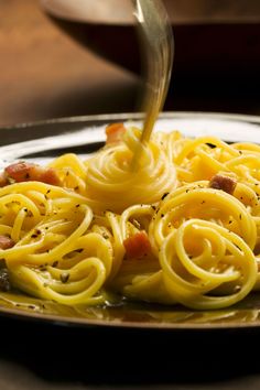 a plate with some noodles and sauce being poured onto it by a fork on the side