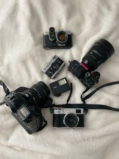 a camera and some other electronic equipment on a white bed sheet with a blanket behind it