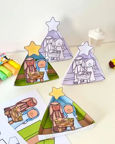 three paper christmas trees with nativity pictures and crayons on the table next to them