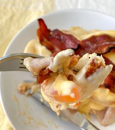 a white plate topped with eggs and bacon next to a fork on a yellow table cloth