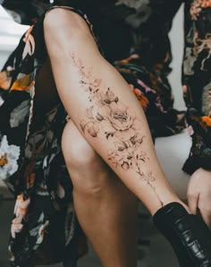 a woman is sitting on the ground with her legs crossed and flowers tattooed on her leg