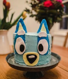 a blue dog cake on a plate with flowers in the background