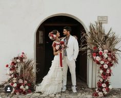 a man and woman standing in front of a doorway with flowers on the ground next to each other