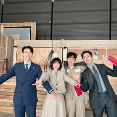 four people posing for a photo in front of wooden planks with their hands up