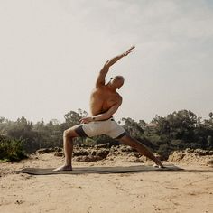 a shirtless man doing yoga on a mat in the middle of a dirt field